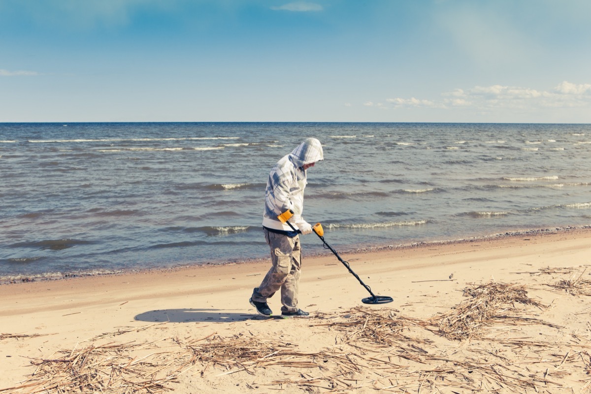 man using a metal detector on the beach