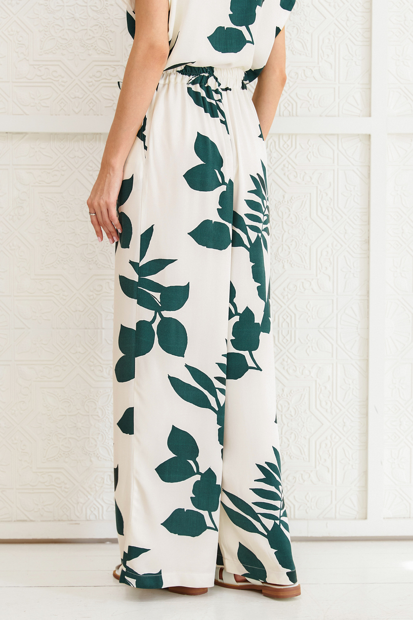 Cropped rear view of a woman wearing a matching palazzo pant and top, cream colored with green leaves print