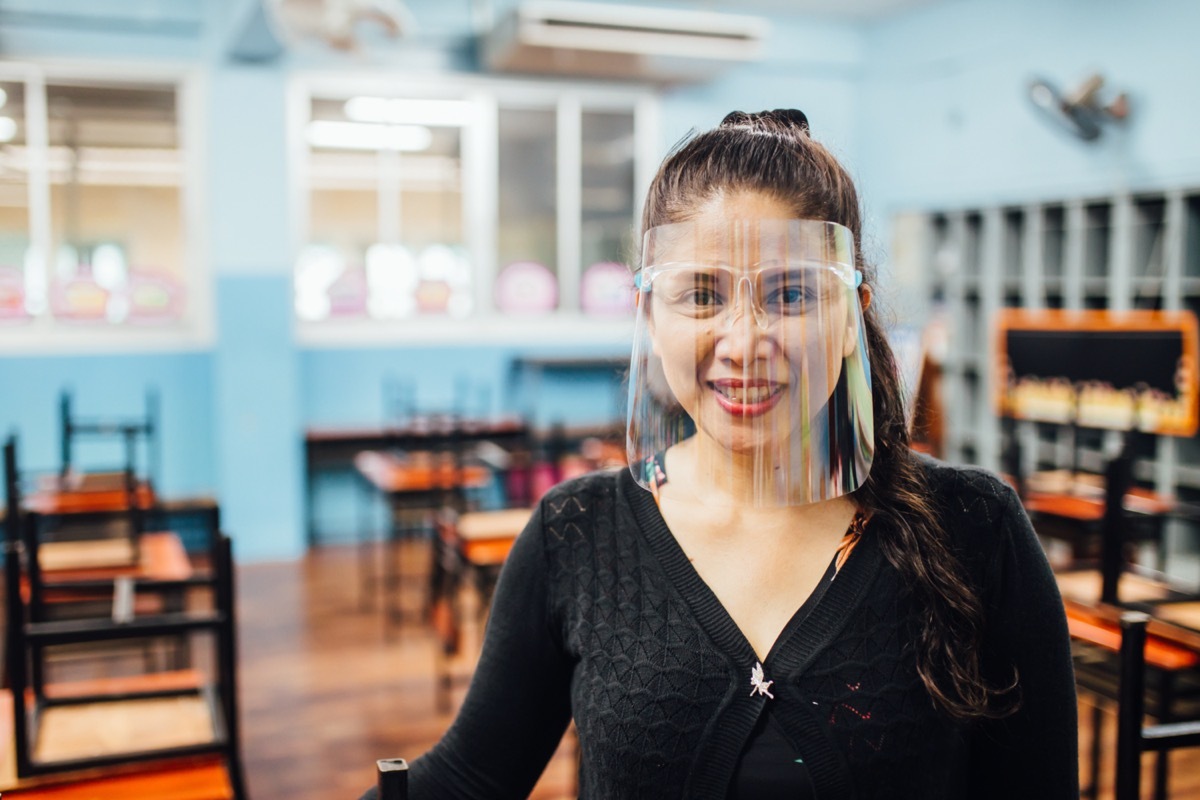 female teacher wearing face shield smiling while standing in classroom