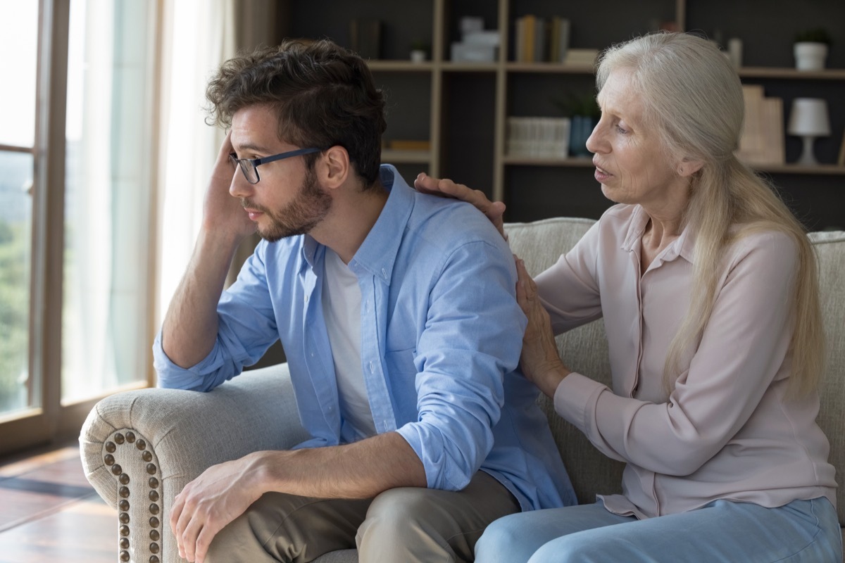 older woman comforting her upset young adult son, gives wise advice in difficult life situation, talking, provide psychological support showing care seated on couch, spend time together at home