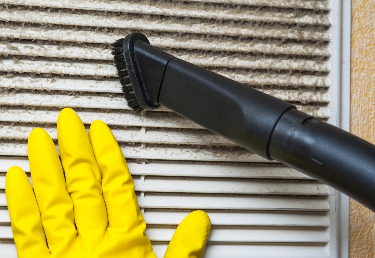 Hand in yellow glove and vacuum cleaner pipe. Ventilation grill cleaning