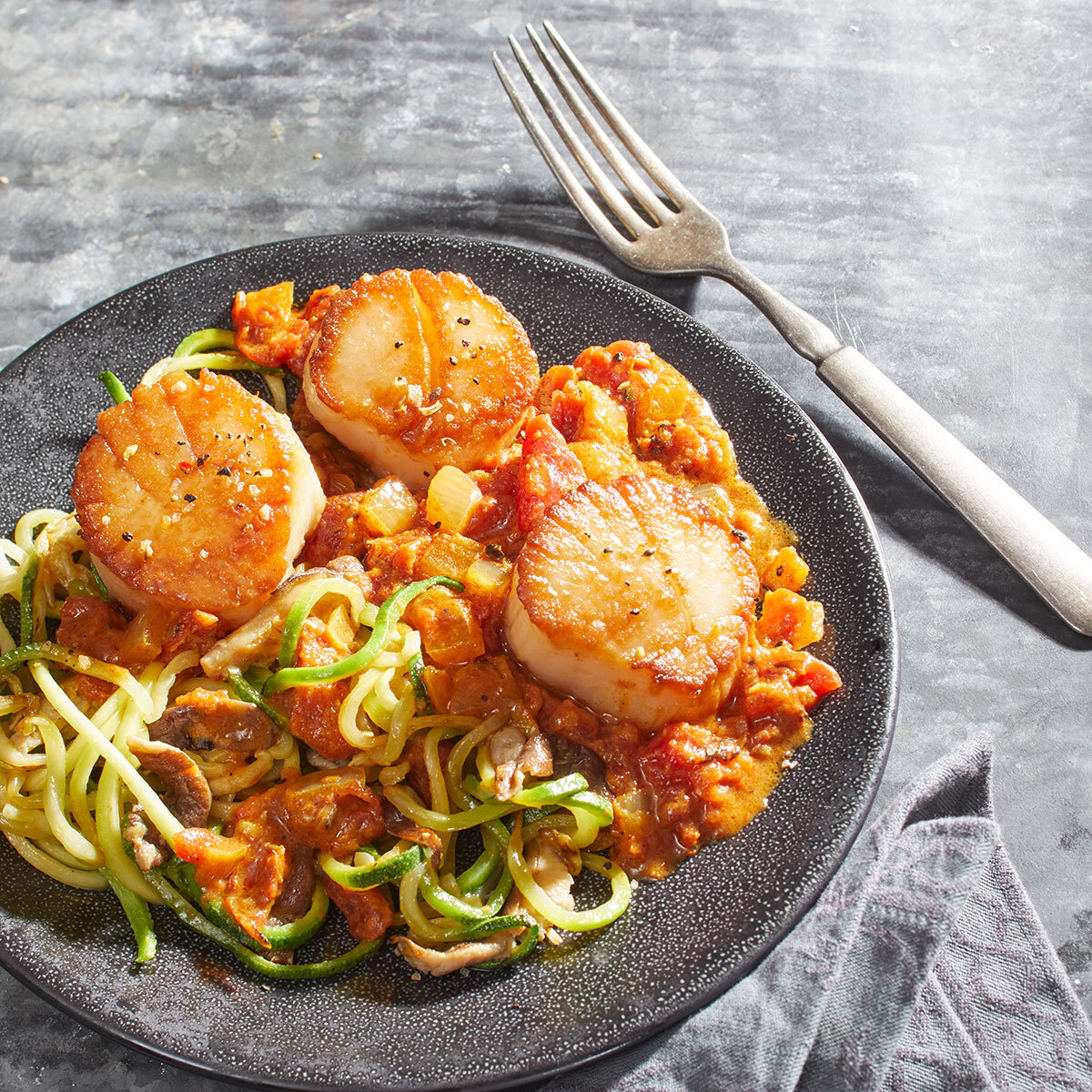 Keto Thai curry with scallops, zucchini noodles, and shiitake mushrooms on a gray plate with fork