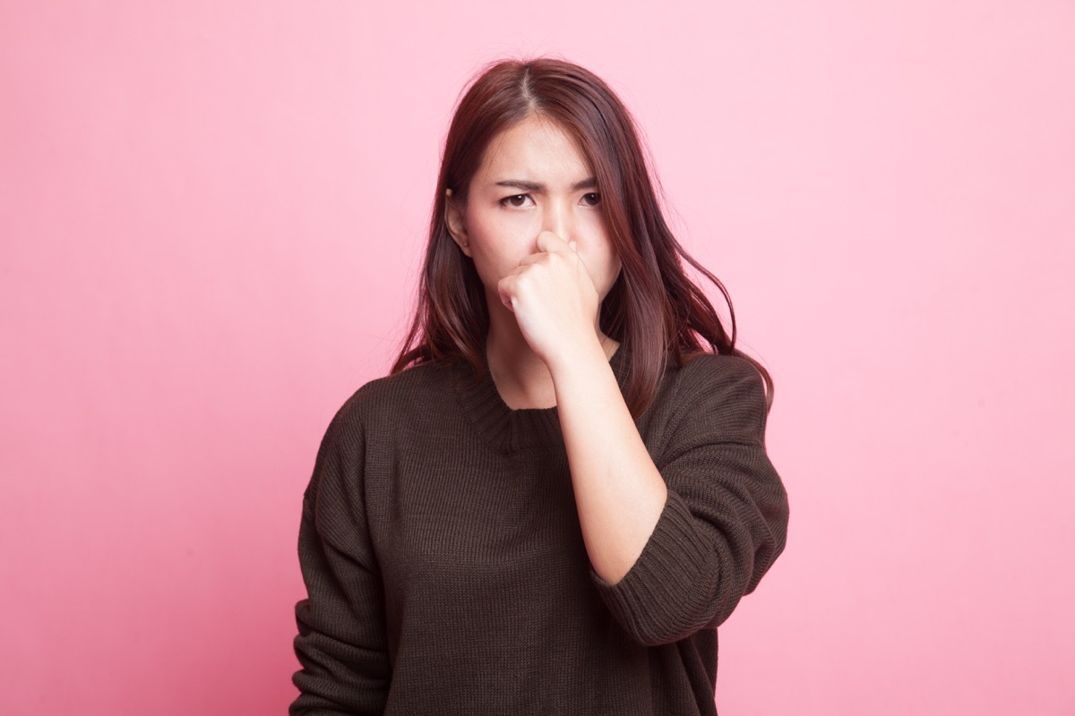 Young Asian woman holding her nose because of a bad smell on pink background - Image