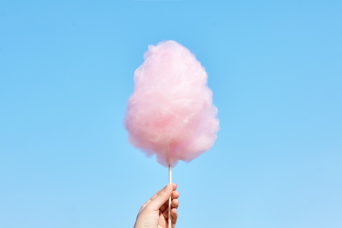 The hands of women holding pink cotton candy in the background of the blue sky