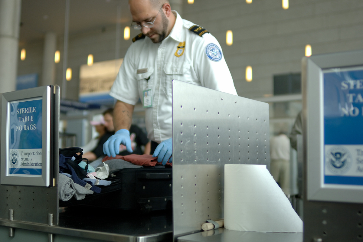 TSA agent scanning luggage through X-ray security checkpoint machine.