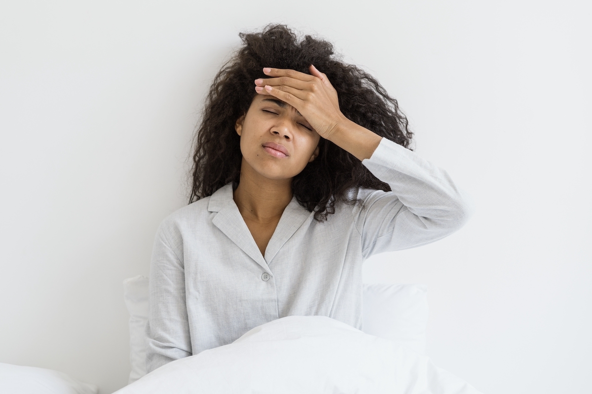 A woman in pajamas sitting up in bed with her hand on her forehand as though she can't sleep