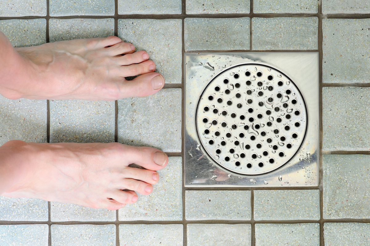 Feet in shower, closeup of floor and drain.