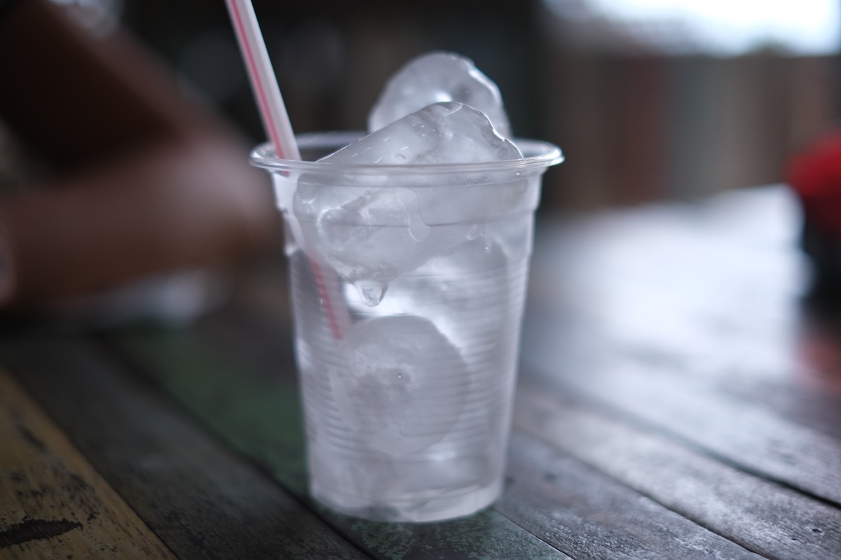 A plastic cup with a straw, full of ice cubes, on a wooden table