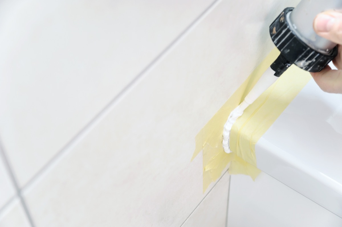 A man is puting the silicone sealant to caulk the joint between a washbasin and a wall.