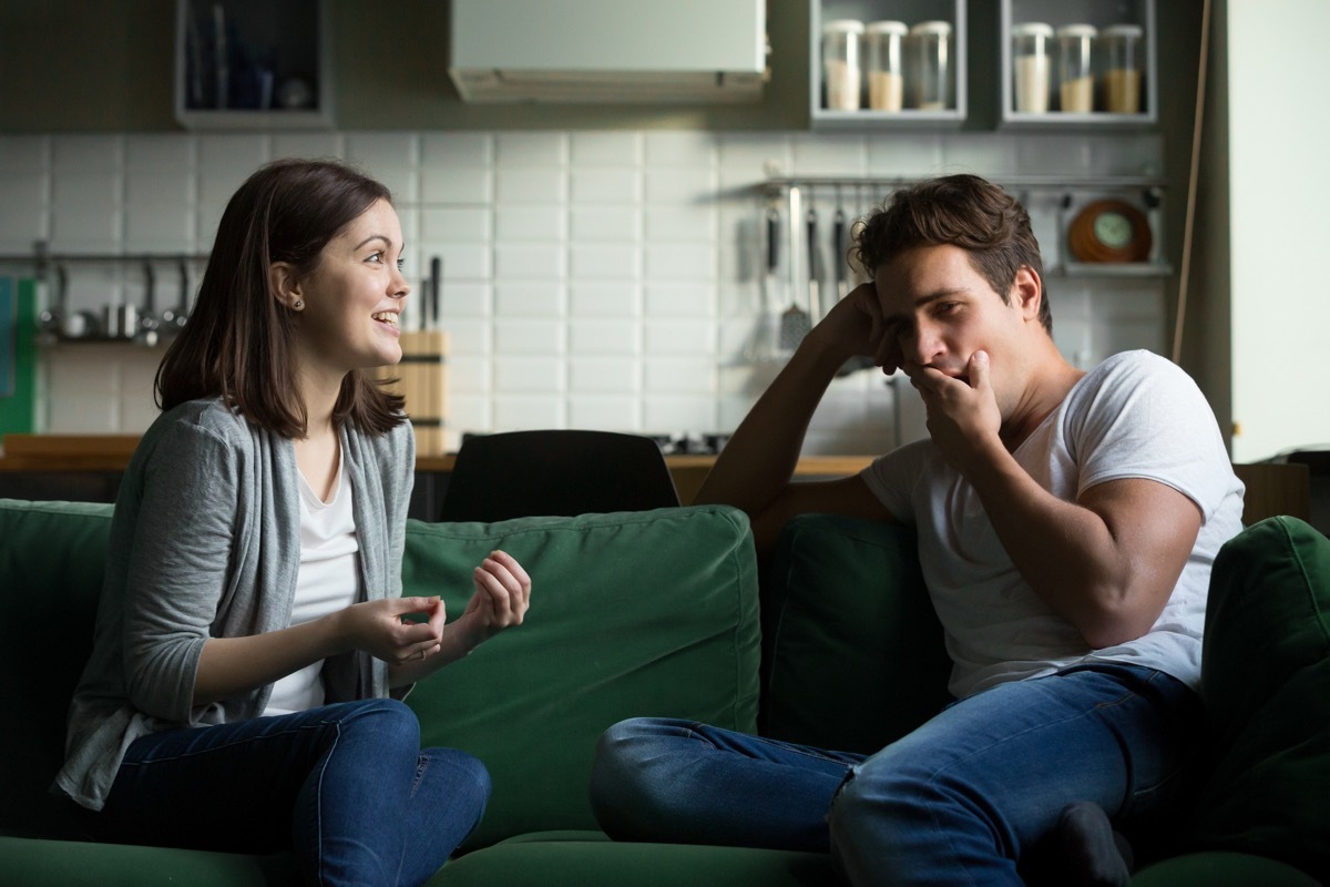 Young husband yawning getting bored listening to excited wife talking for a long time, tired boyfriend not interested in girlfriend gossiping sitting on couch at home, boring conversation concept