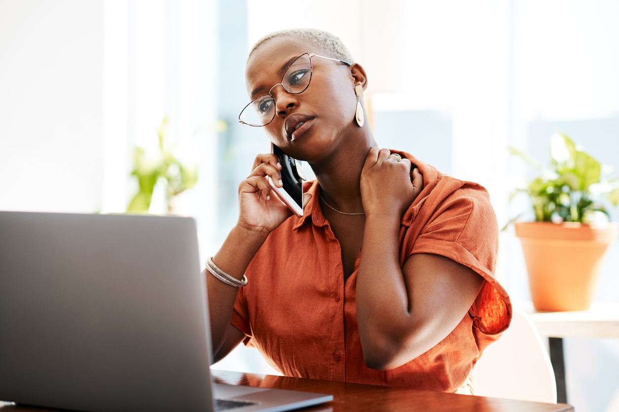 A young woman talking on the phone with a concerned look on her face while sitting in front of a laptop