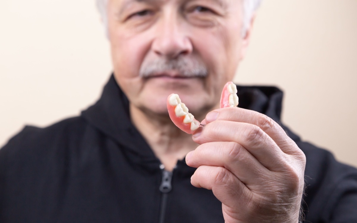 An old gray-haired man holds his denture. The man puts on the denture. Implant. Orthodontics. Old age. Teeth. Jaw. Advertising. The close plan. View from above. Removable denture.