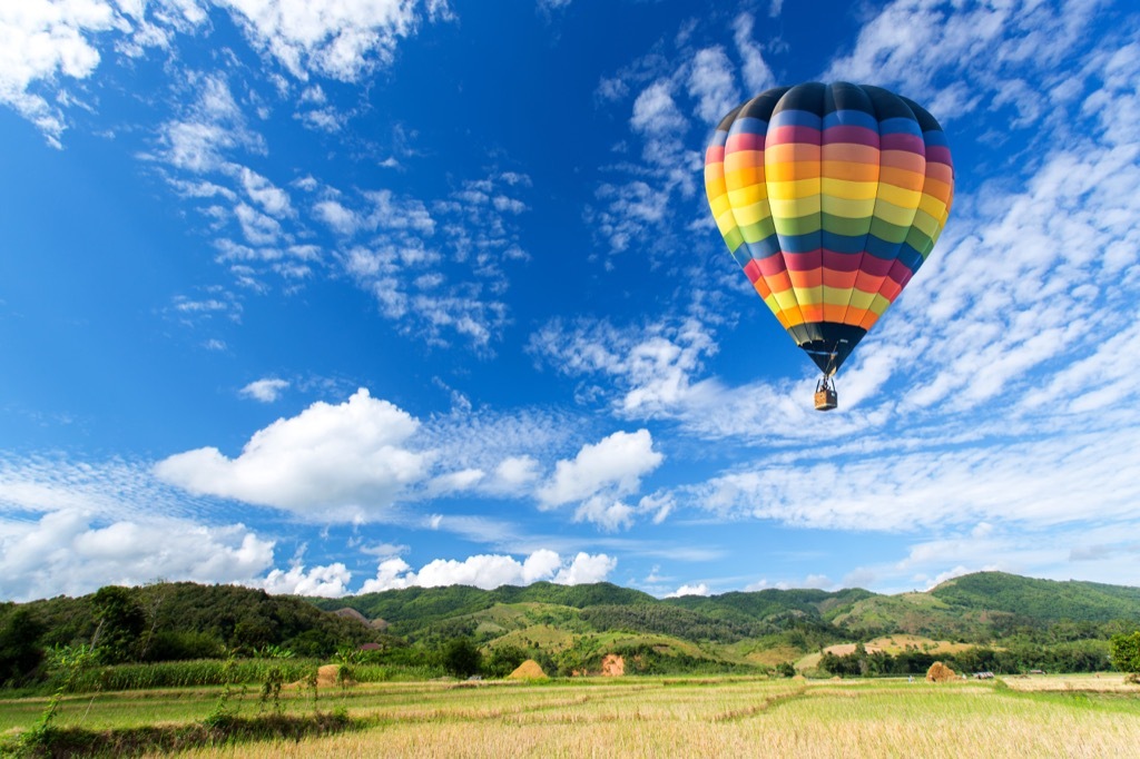 rainbow colored hot air balloon floats amid clouds above a green pasture, state fact about maryland