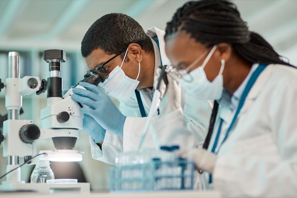 Shot of a young scientist using a microscope while working alongside a colleague in a lab