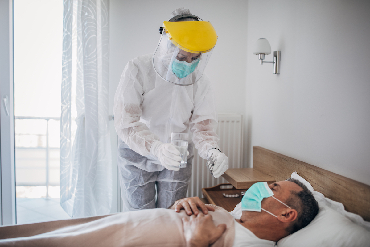 Doctor giving medicine to a man lying in hospital bed because of coronavirus infection