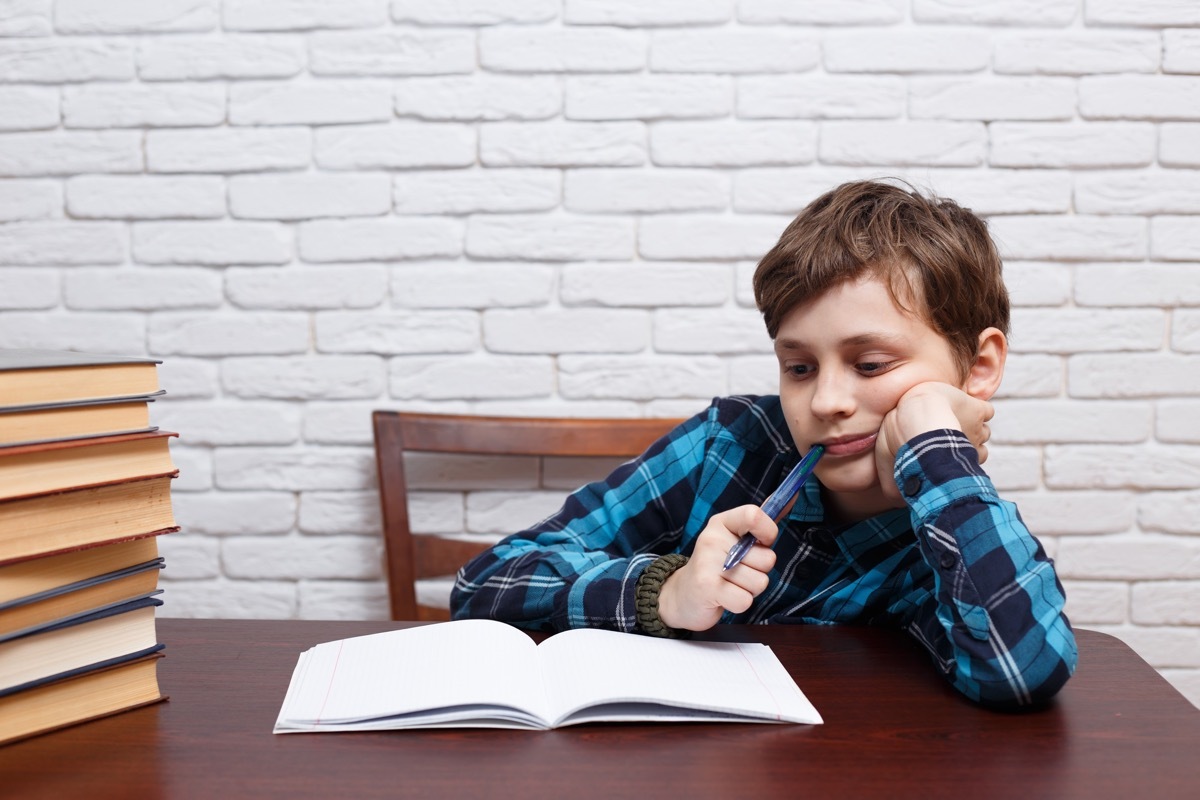 White boy chews pen cap at desk, bad child habit