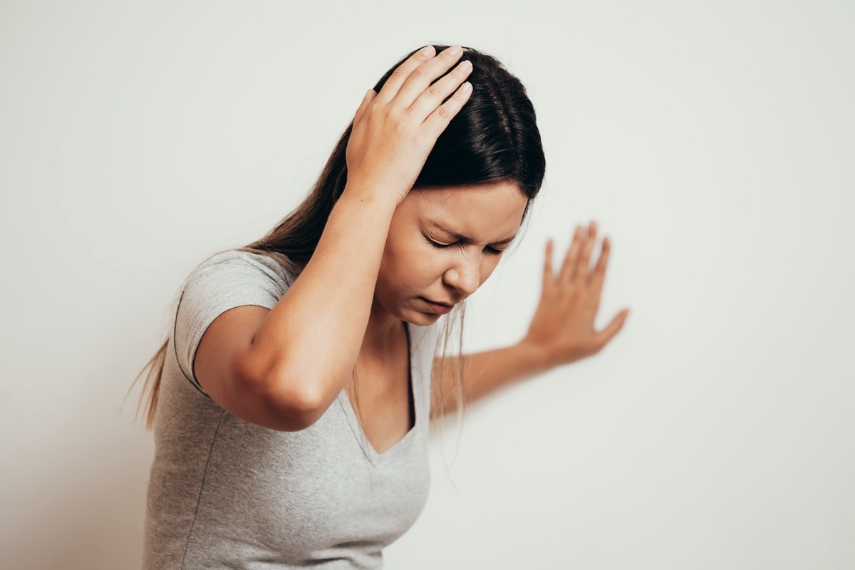 Woman suffering from dizziness with difficulty standing up while leaning on wall